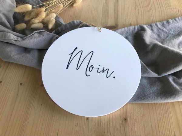 Schild in weiß mit Wort Moin auf einem Tisch