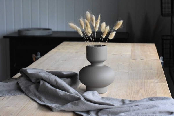 Vase in einem dunklen Farbton mit Trockenblumen auf einem Holztisch