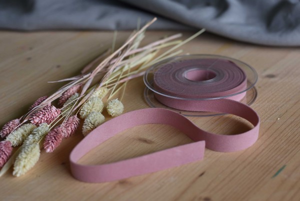 Zweiseitiges Samt-Band in altrosa auf einem Holztisch mit Trockenblumen in rosa und beige