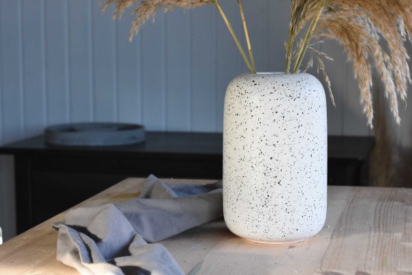 Vase in weiß mit schwarzen feinen Punkten mit Trockenblumen auf einem Holztisch
